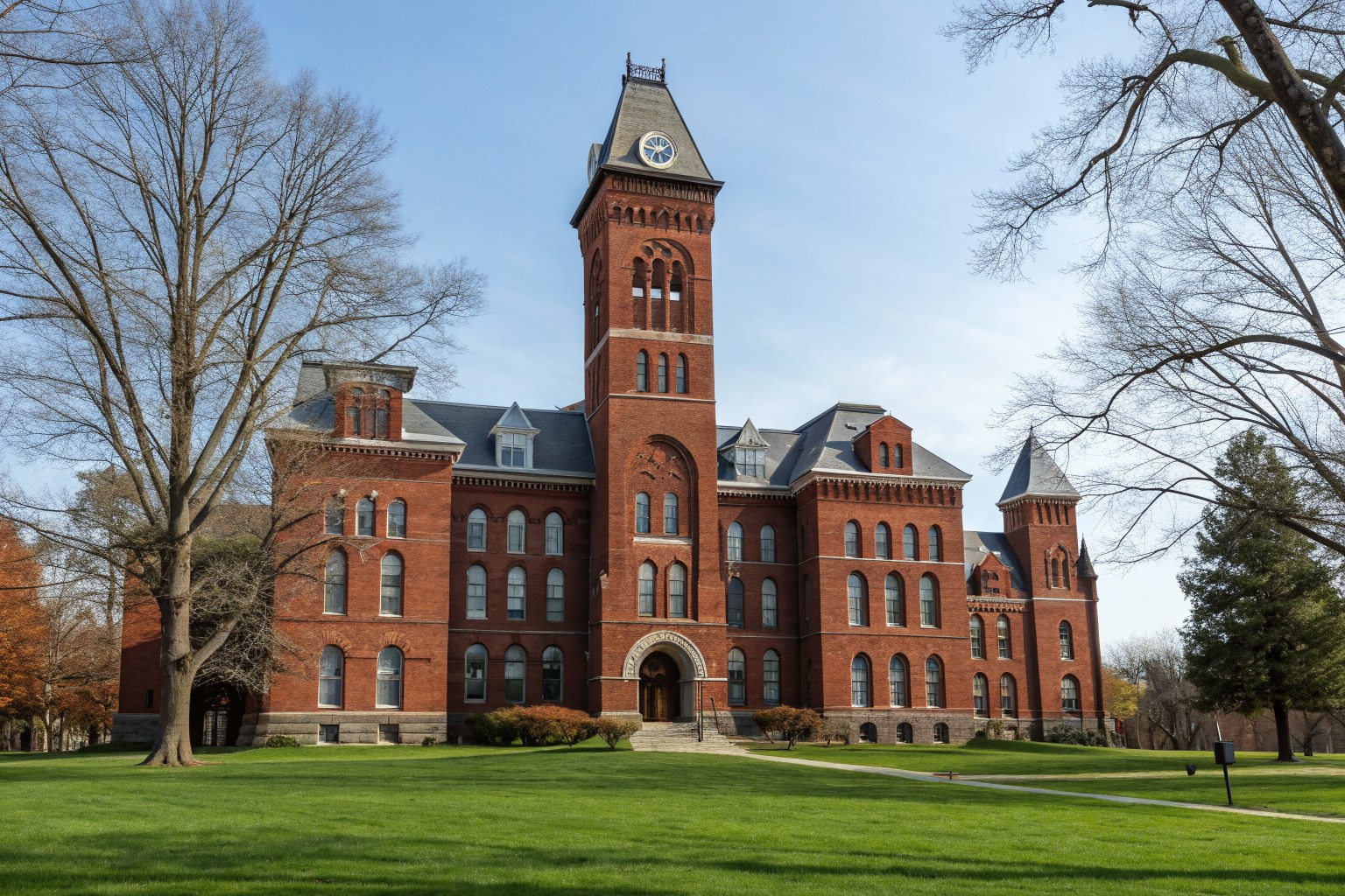 A historic red brick college hall with a tall tower on a green lawn