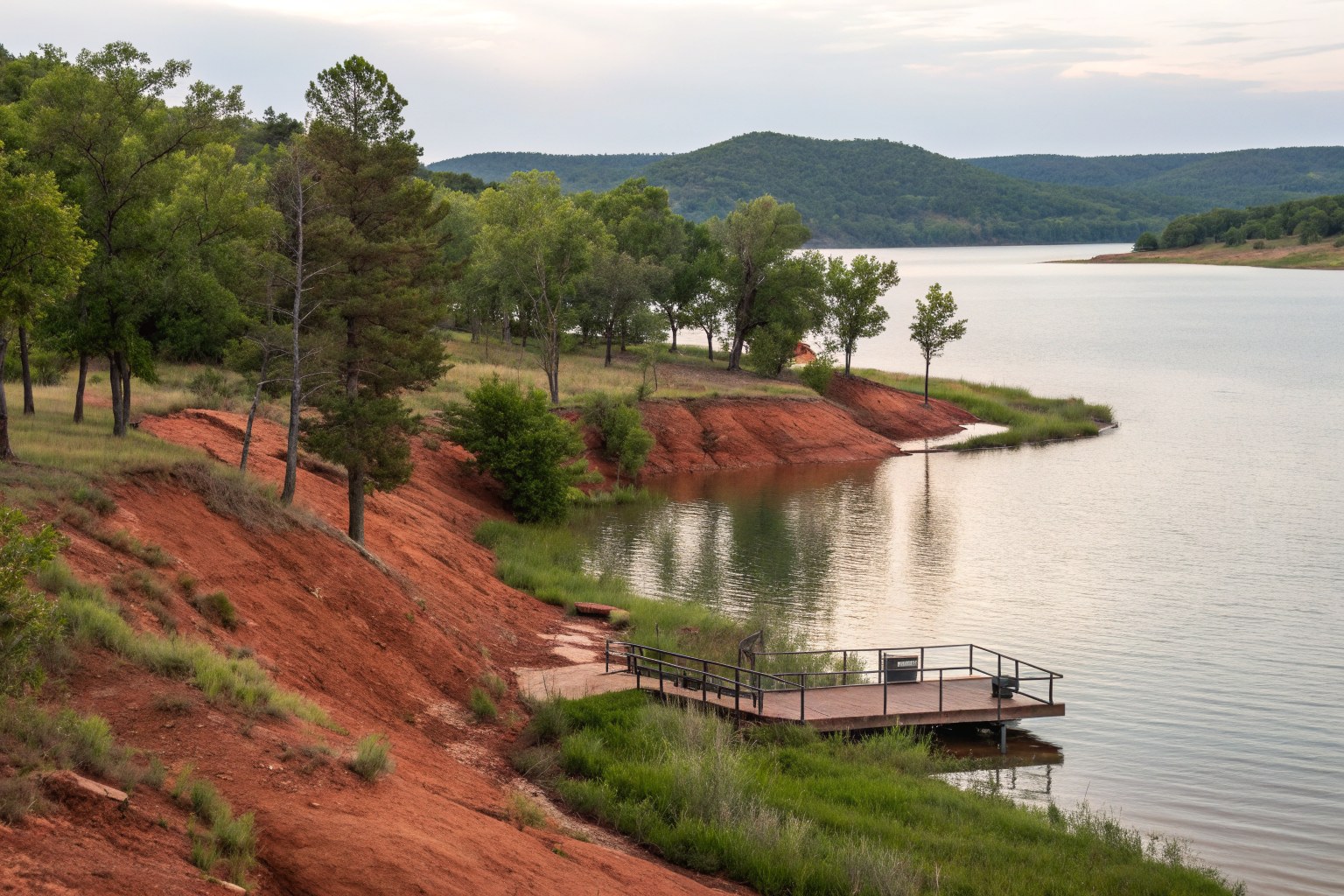 A calm lake with red clay banks, a small dock and wooded hills